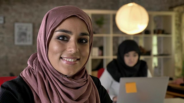 年轻的穆斯林妇女戴着头巾工作、思考，两个妇女坐在现代办公室的笔记本电脑上打字视频素材