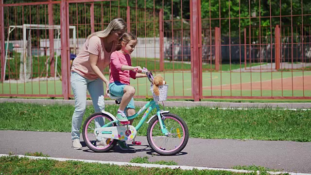 一个女人和她的女儿玩，教她骑自行车视频素材