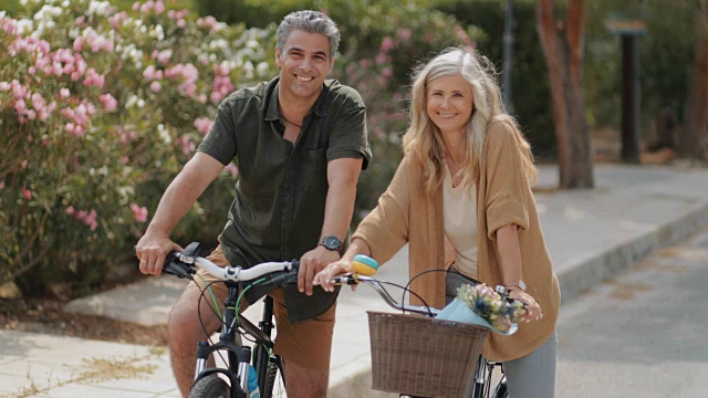 微笑的多民族成熟夫妇在公园里一起骑自行车视频素材