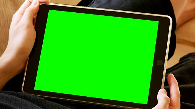 男人躺在沙发上，拿着绿色屏幕的数字平板电脑视频素材