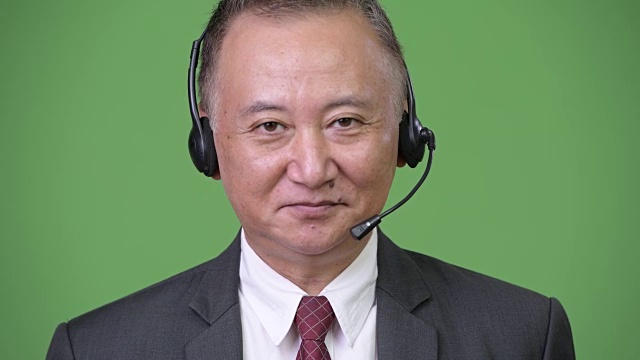 在绿色背景下作为呼叫中心代表的成熟日本商人视频下载