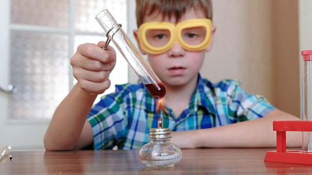 在家做化学实验。男孩在燃烧的酒精灯上用红色液体加热试管。液体沸腾。视频下载