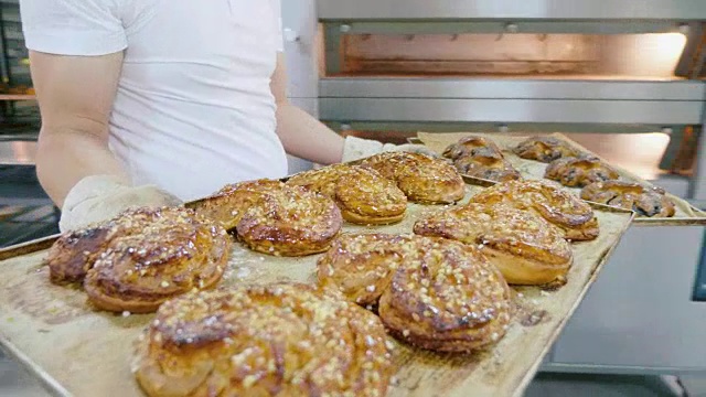 专业的面包师在商业厨房里把甜面包从烤箱里拿出来视频素材