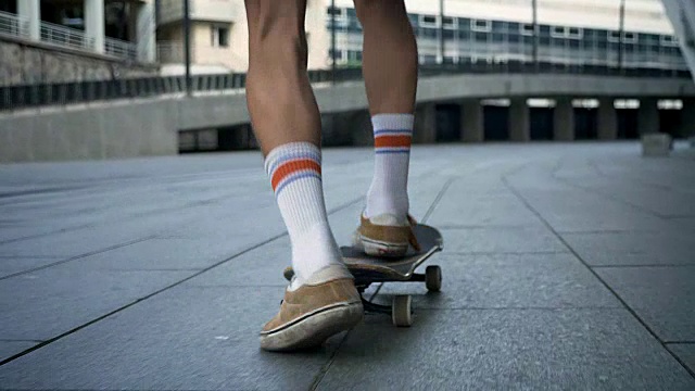 滑板者的脚在城市溜冰时，男性的腿在滑板上做把戏，从后面看视频素材