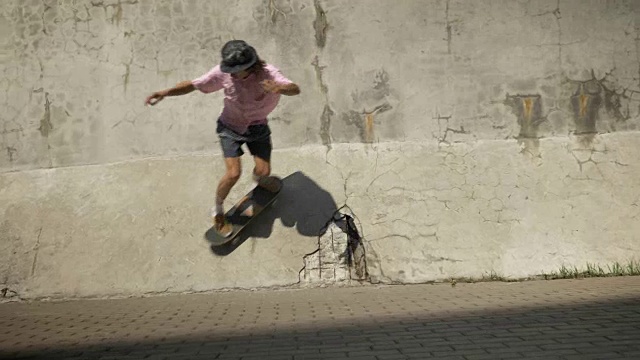 时髦的滑板手在旧墙上玩滑板把戏视频素材