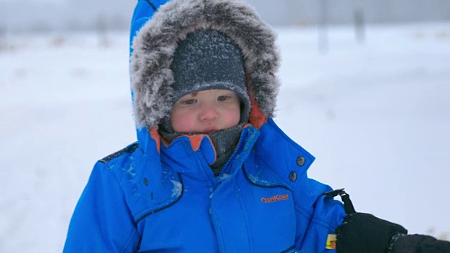 可爱的小男孩在暴风雪中穿着皮大衣视频素材