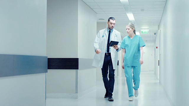 外科医生和女医生走在医院走廊上，一边谈论病人的健康，一边咨询数字平板电脑。拥有专业人员的现代光明医院。视频素材