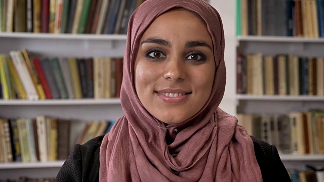 年轻美丽的穆斯林妇女戴着头巾，微笑着看着镜头，站在图书馆视频下载
