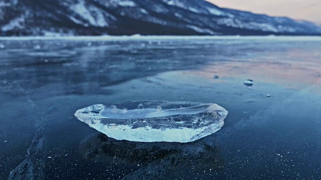 浮冰在冰面上旋转，映衬着令人惊叹的山景。缓慢的运动。镜头移到了冰的后面。冰在冰上旋转，有神奇的裂缝，非常漂亮。视频素材