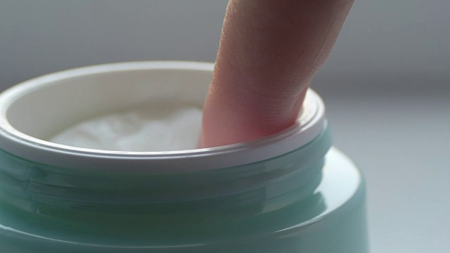 绿色的罐子里装有温和的化妆品面霜，女性用手指触摸面霜近观。奶油宏指出视频素材
