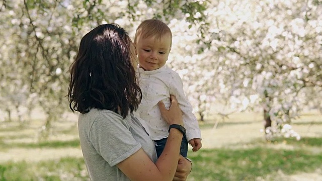 年轻的母亲和婴儿一起在户外欢笑。母亲亲吻小儿子视频素材