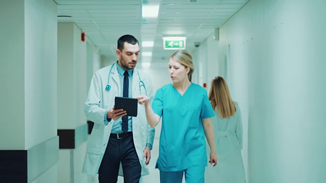 女外科医生和女医生走在医院的走廊上，一边看数字平板电脑，一边谈论病人的健康。拥有专业人员的现代光明医院。视频素材