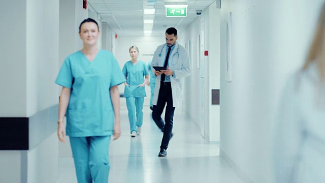 坚定英俊的医生用平板电脑慢镜头走过医院走廊。拥有专业人员的现代光明诊所。视频素材