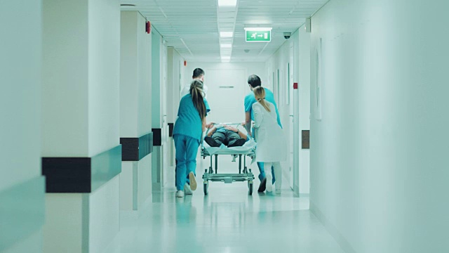 急诊科:医生，护士和护理人员推动轮床/担架与严重受伤的病人走向手术室。明亮的现代医院，专业人员挽救生命。视频素材
