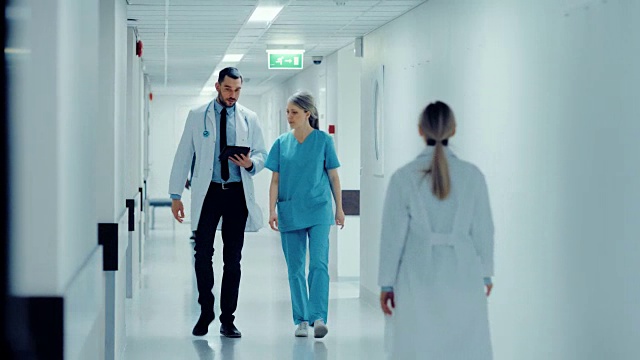 女外科医生和医生走在医院走廊上，一边看数字平板电脑一边谈论病人的健康。拥有专业人员的现代光明医院。视频素材