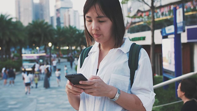 美丽的亚洲女人穿着白衬衫，在香港旅行时使用智能手机视频素材