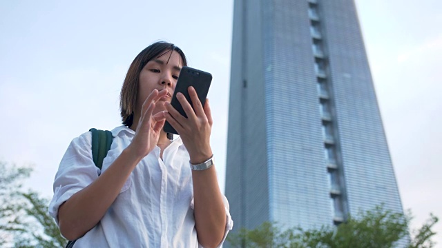 美丽的亚洲女人穿着白衬衫，在香港旅行时使用智能手机视频素材