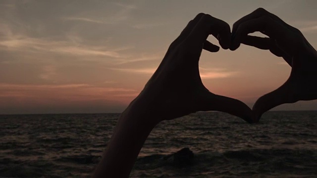 夕阳西下，女子双手做心形手势，女孩高举爱的象征视频素材