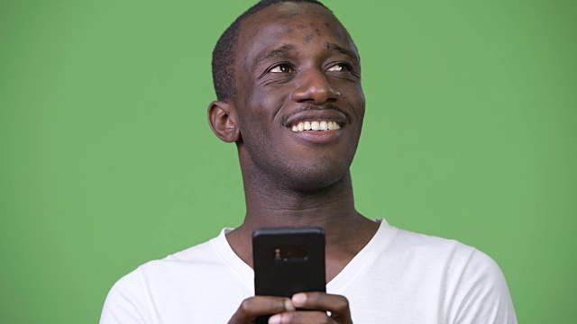 年轻的非洲男子在绿色背景下用手机思考视频素材