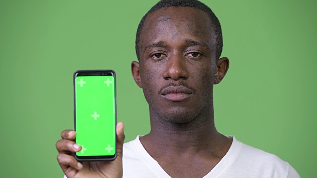 年轻的非洲男子在绿色背景下展示手机视频素材