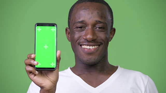 年轻快乐的非洲男子微笑着向镜头展示手机视频素材