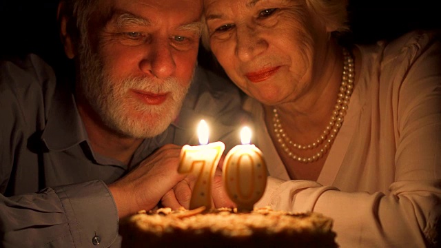 相爱的老年夫妇晚上在家用蛋糕庆祝结婚纪念日。吹灭蜡烛视频购买