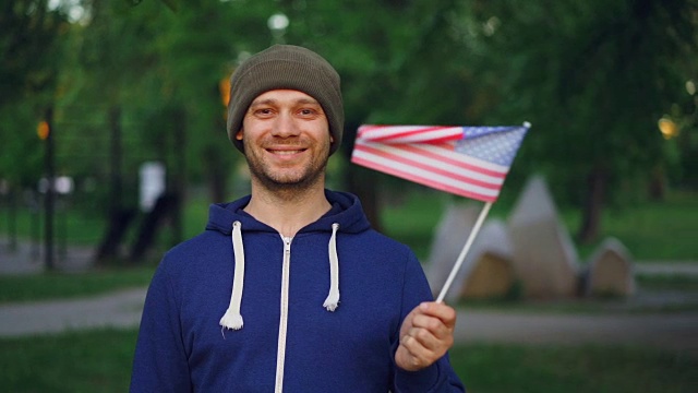 慢动作肖像的蓄着胡子的美国人骄傲的公民挥舞着美国官方旗帜，看着镜头与高兴的微笑。人、国家和景观的概念。视频下载