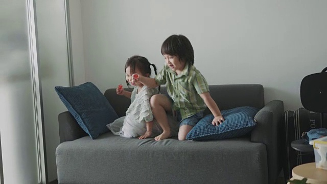 泰国可爱的小女孩和蹒跚学步的男孩在客厅的沙发上跳舞和玩耍-库存视频视频素材