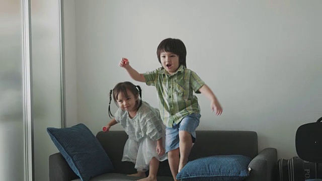 泰国可爱的小女孩和蹒跚学步的男孩在客厅的沙发上跳舞和玩耍-库存视频视频素材
