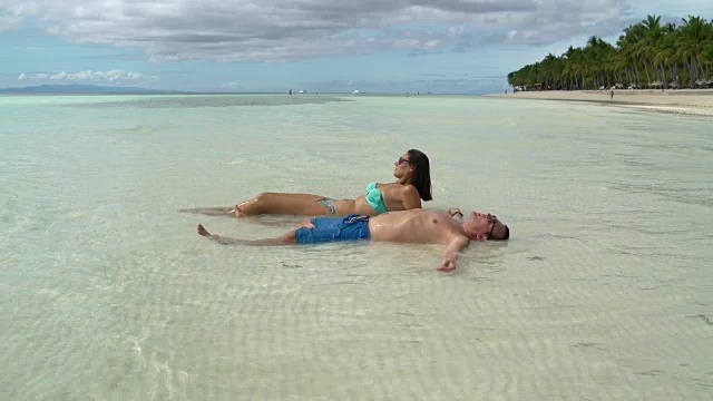 一个穿泳衣的女人和一个穿短裤的男人躺在海边晒太阳视频下载