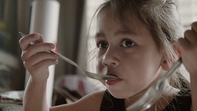 快乐的女孩用勺子吃着美味的食物。视频下载
