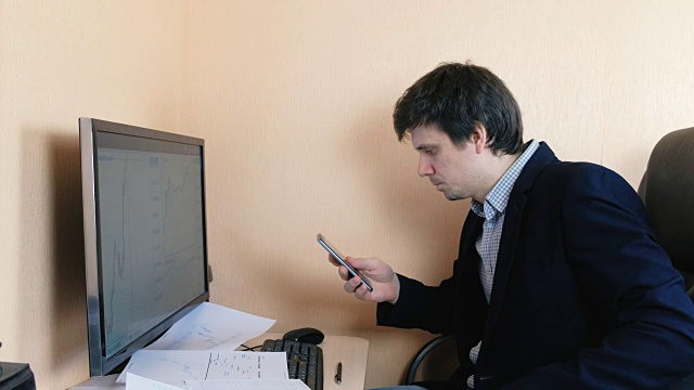 男人正在浏览他的手机在电脑上工作。视频素材