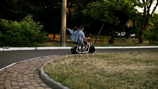 一对快乐的年轻夫妇在公园边骑着一辆小型自行车。女孩感觉很好，伸出双手。背后的观点视频下载