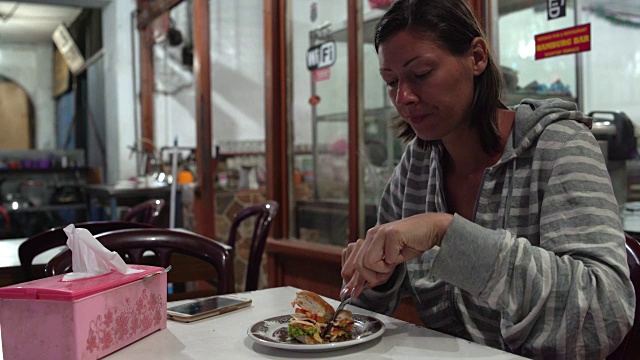 一个女人在咖啡馆里用刀叉吃汉堡包视频素材