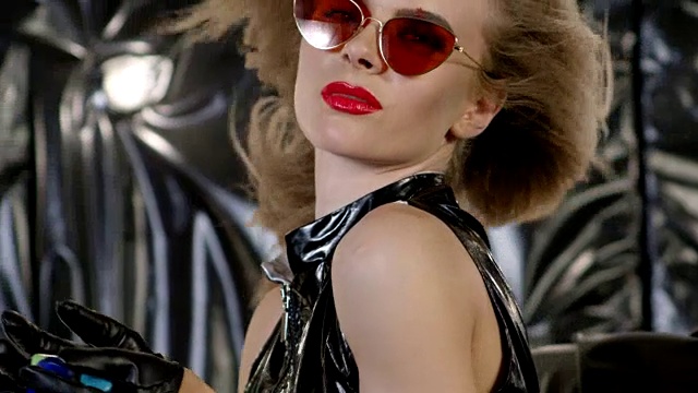 一个时尚模特的特写，戴着墨镜和黑色皮手套，拿着多种颜色的指甲油瓶子。时尚视频。视频素材