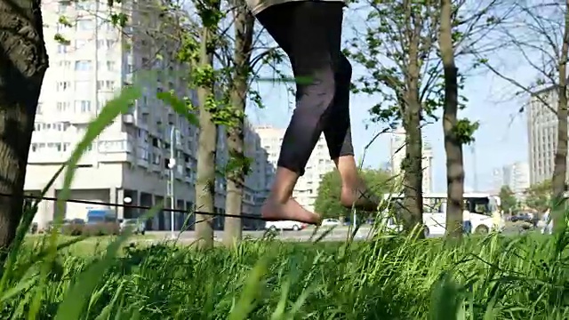 一个欧洲女孩在城市公园里走钢丝。女人在松紧带上保持平衡，特写视频下载