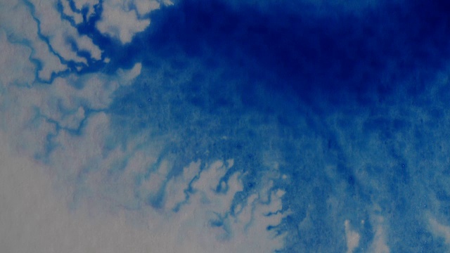 蓝色墨水滴在潮湿的水彩纸上的特写。视频下载