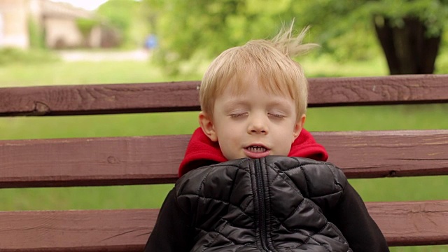 一个微笑的男孩在公园的长椅上的肖像。视频素材
