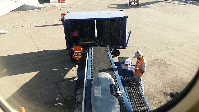 从飞机窗口拍摄的慢动作剪辑行李搬运人员在装载行李，货物在卸货视频下载