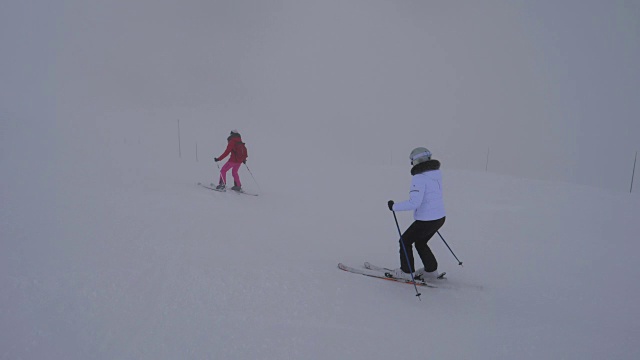 两名女滑雪者在冬季大雾中下坡滑雪视频下载
