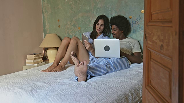 多民族年轻夫妇在床上浏览网络视频下载
