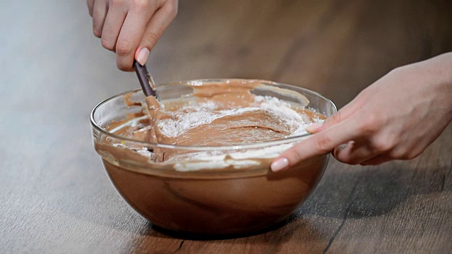 糕点师在煮生面团。在烤巧克力饼干蛋糕时，一只手用塑料抹刀在一个钢碗里搅拌面团视频下载