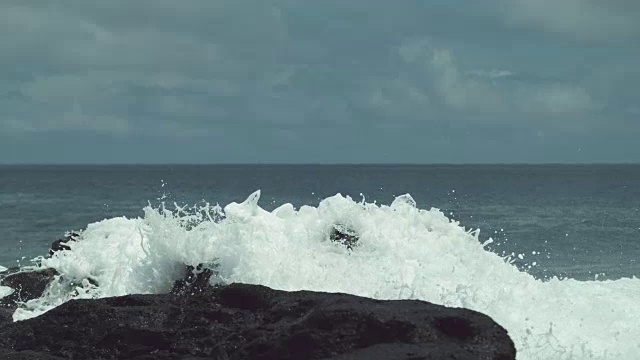 慢动作:强大的海浪冲击着黑色的岩石海岸，在空中溅起水花视频素材
