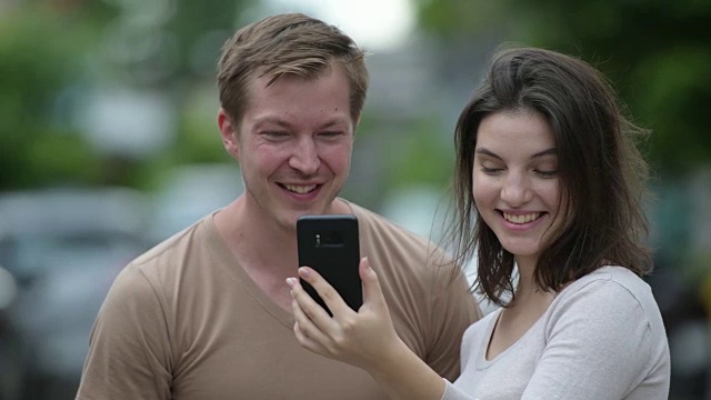 一对年轻幸福的夫妇在户外的街道上一起使用手机视频下载