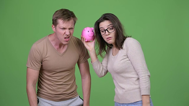 一对年轻夫妇在绿色的背景下一起摇晃存钱罐视频下载