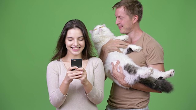 一对年轻夫妇在绿色背景下和猫一起使用手机视频下载