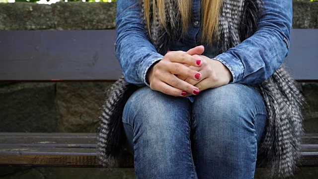 在秋天的公园里，一个女人坐在长椅上，双手紧张视频素材