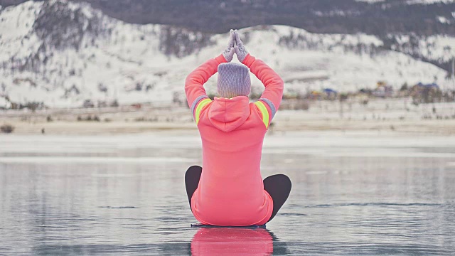 女孩在冬天练习瑜伽。女人在大自然的冰上做伸展和冥想。运动员练习瑜伽在美丽的裂缝冰。女人在户外做运动健身。视频下载
