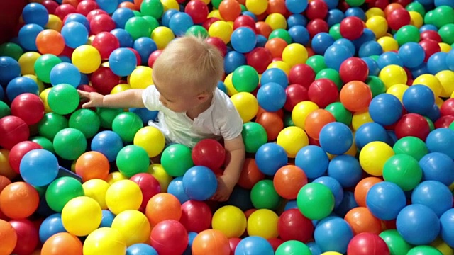 可爱的蹒跚学步的小男孩，在室内的儿童操场上玩五颜六色的球视频下载