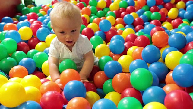 可爱的蹒跚学步的小男孩，在室内的儿童操场上玩五颜六色的球视频下载